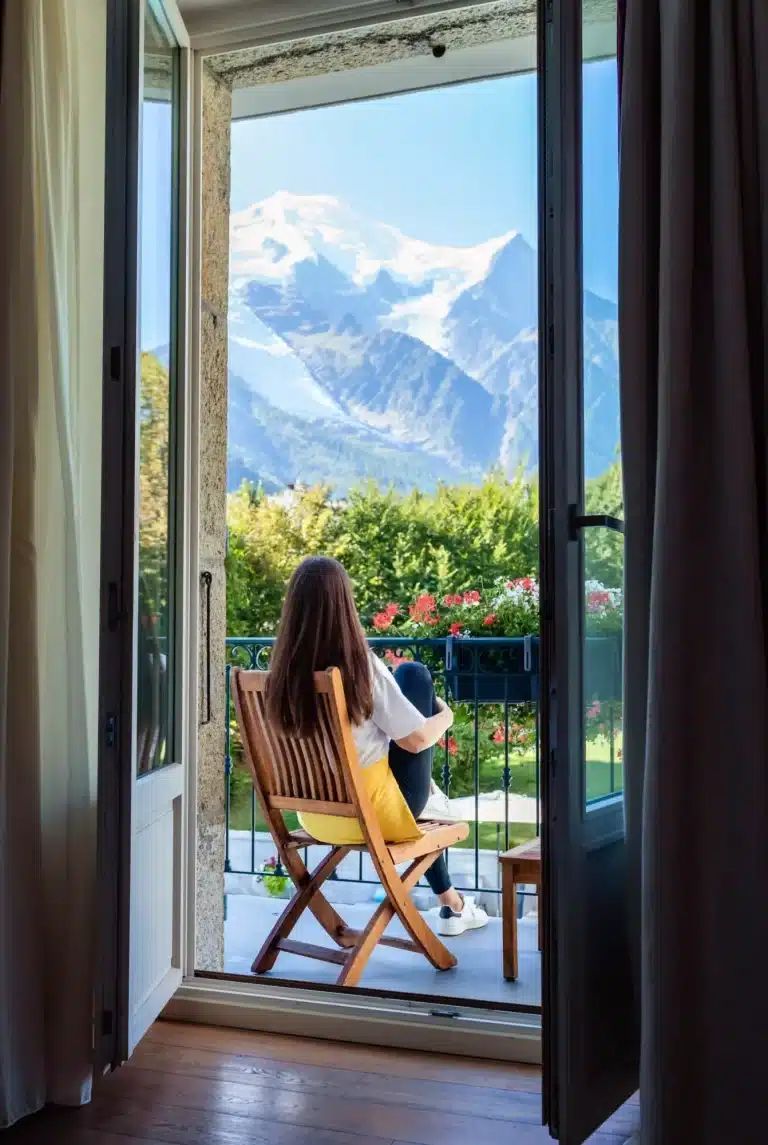 Schönes junges Mädchen mit langen Haaren entspannt sich, trinkt Tee und genießt die herrliche Aussicht auf den Mont Blanc auf dem Balkon am Morgen.